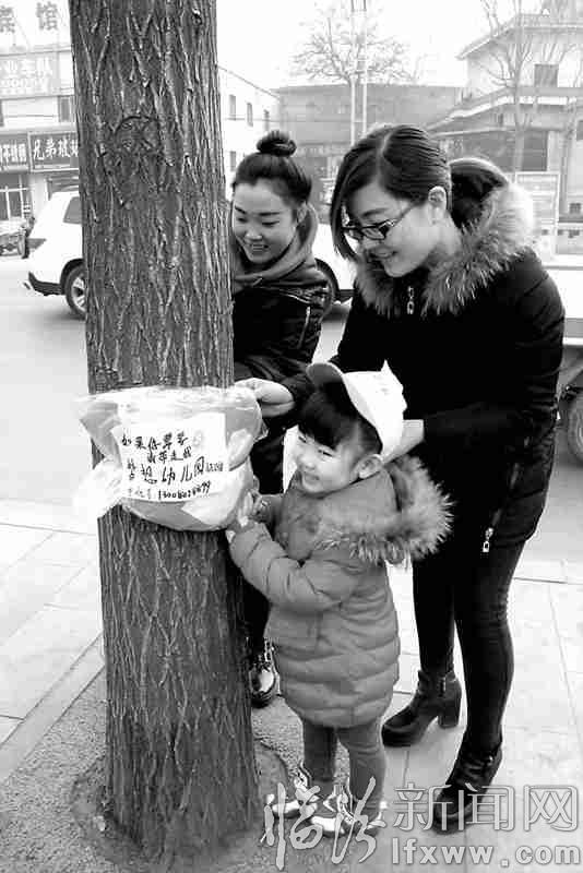 孩子在老師和家長的幫助下,把捐贈衣物綁在樹上。